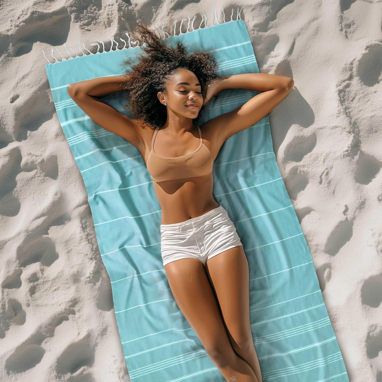 Aqua and white striped Cacala hammam towel spread out on a sandy beach