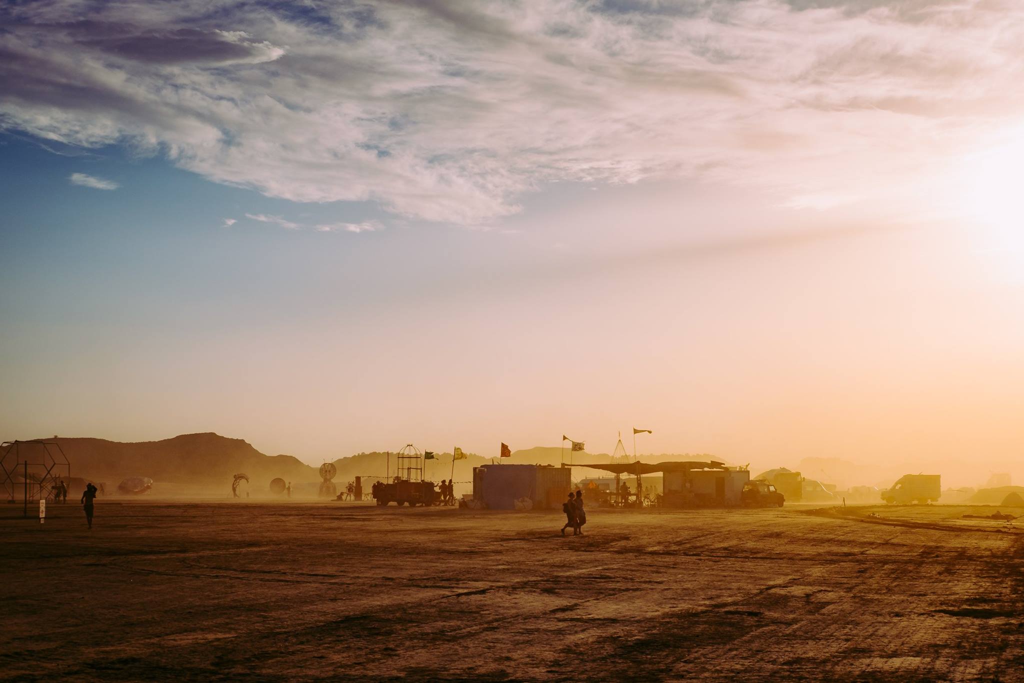 Sunset over dusty Nowhere camp, with silhouettes and low structures beneath a pastel sky