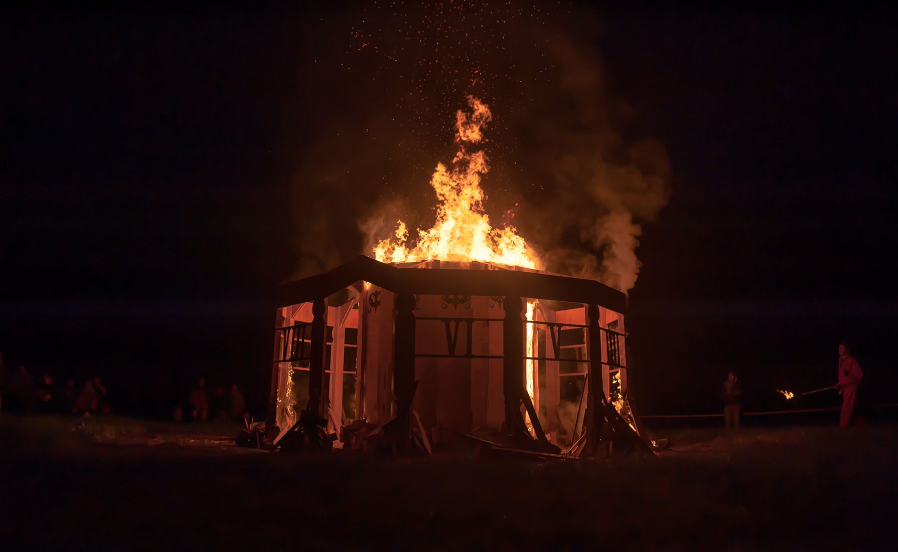 A wooden structure burns at night at Burning Nest. The source does not state the edition.