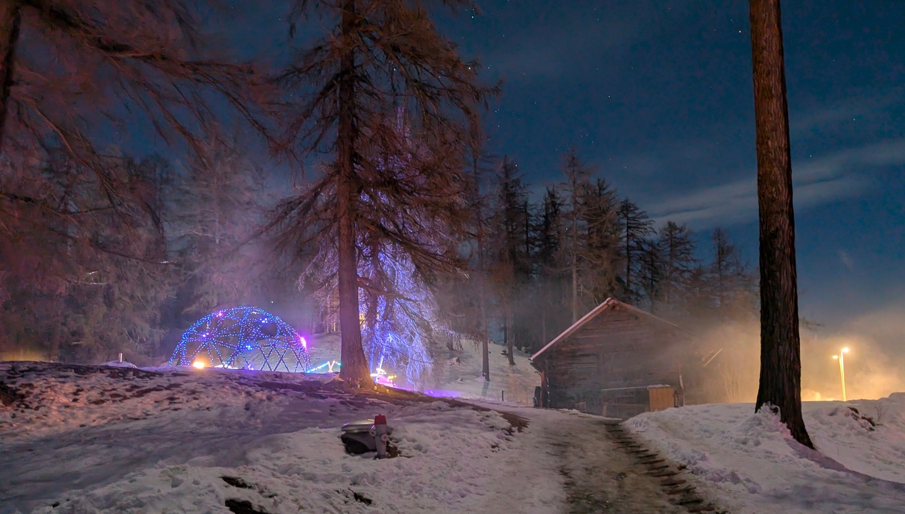An illuminated dome and cabin among snow-covered trees at the Swiss Winter Burn.