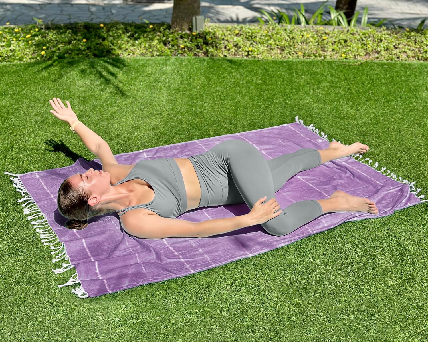 Manufacturer photograph of a woman lying on one purple Utopia towel spread on grass